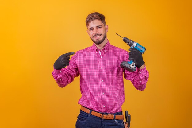 Positieve en zelfverzekerde reparateur in een geruit overhemd en een gereedschapskist op zijn heup en een elektrische schroevendraaier die lacht en naar de camera kijkt