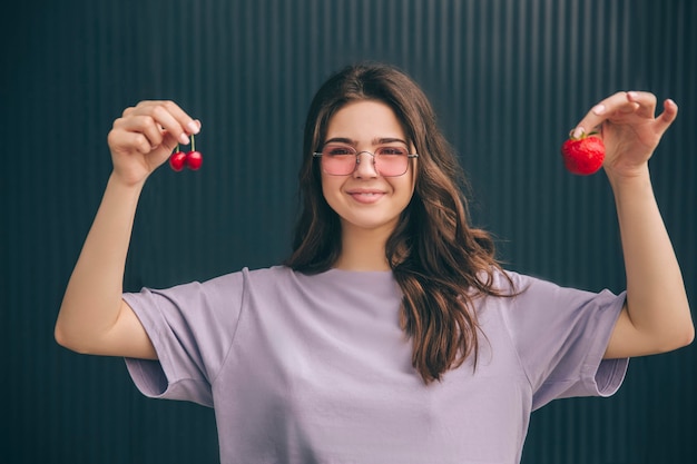 Positieve gelukkige vrolijke vrouw met kersen en aardbei in handen en tonen