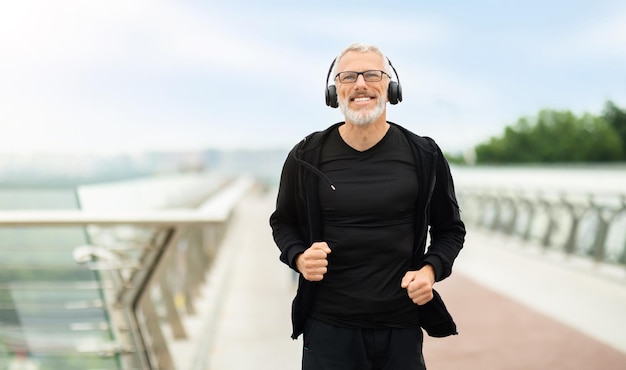 Positieve gepensioneerde sporter die jogt door naar muziek te luisteren