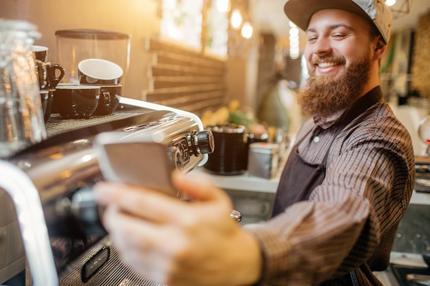 Foto positieve jonge barisa selfie te nemen op de werkplek. hij stond keuken bij koffiemachine. guy is blij.