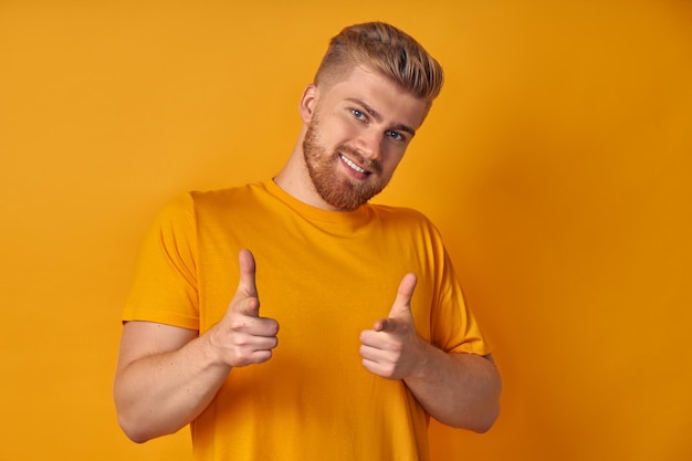 Positieve jonge lachende man met baard wijst wijsvingers naar de camera kiest je glimlacht breed