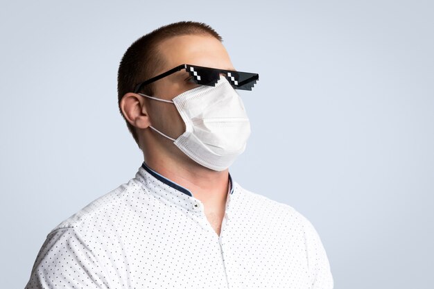 Positieve jonge man met pixel zonnebril en hygiënisch masker om infectie, luchtwegaandoeningen zoals griep, 2019-nCoV op blauw geïsoleerd te voorkomen