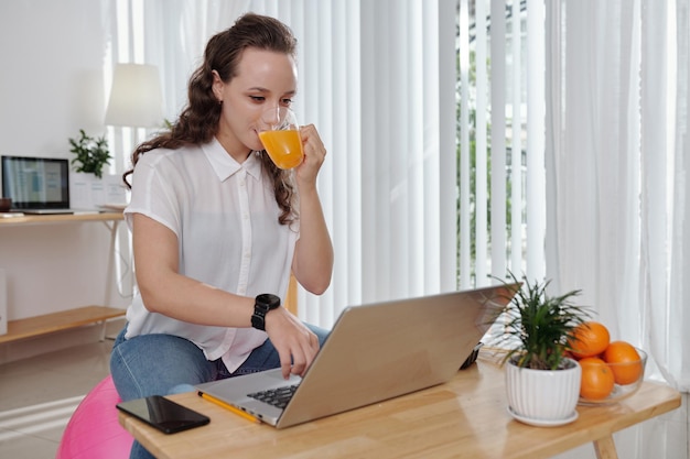 Positieve jonge student die sap drinkt en online webinar op laptopscherm kijkt