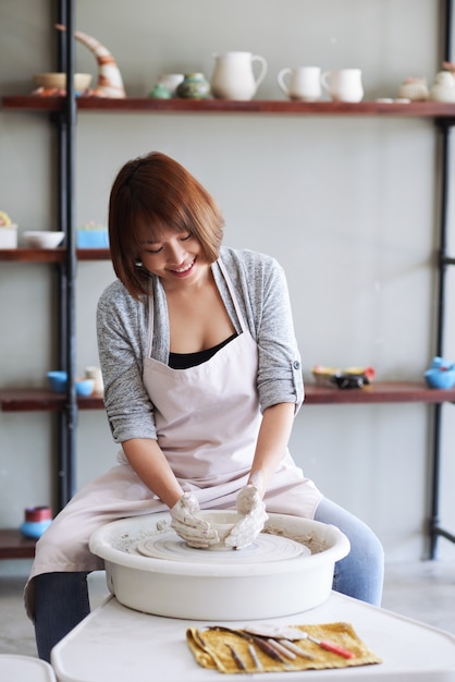 Positieve jonge Vietnamese vrouwelijke keramist die kleiproduct maakt op pottenbakkerswiel in studio