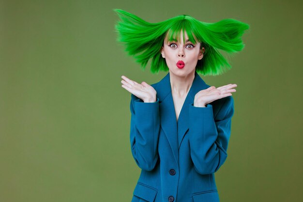 Positieve jonge vrouw aantrekkelijke look groene pruik blauwe jas poseren groene achtergrond ongewijzigd