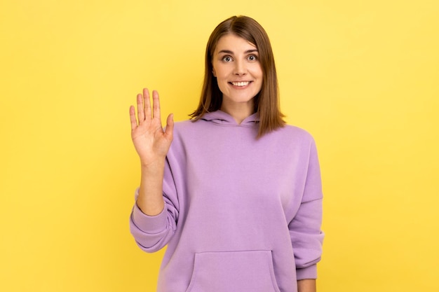 Positieve jonge vrouw glimlacht tandjes omhoog, handpalm begroet vriend die hallo of tot ziens zegt