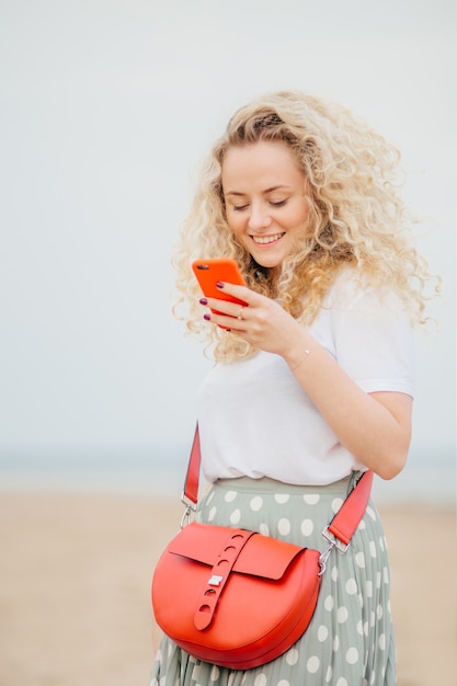 Positieve jonge vrouw maakt gebruik van moderne slimme telefoon, heeft een vrolijke uitdrukking, maakt online winkelen.