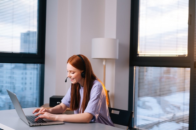 positieve jonge vrouw operator met behulp van headset en laptop tijdens klantenondersteuning op kantoor aan huis.