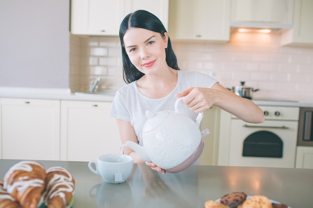 Positieve jonge vrouw zit aan tafel in de keuken