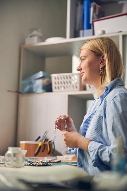 Positieve juweelmedewerker die recht kijkt terwijl hij een stijlvolle ketting met parels vasthoudt