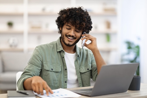 Positieve knappe Indiase man die online werkt en een telefoongesprek voert