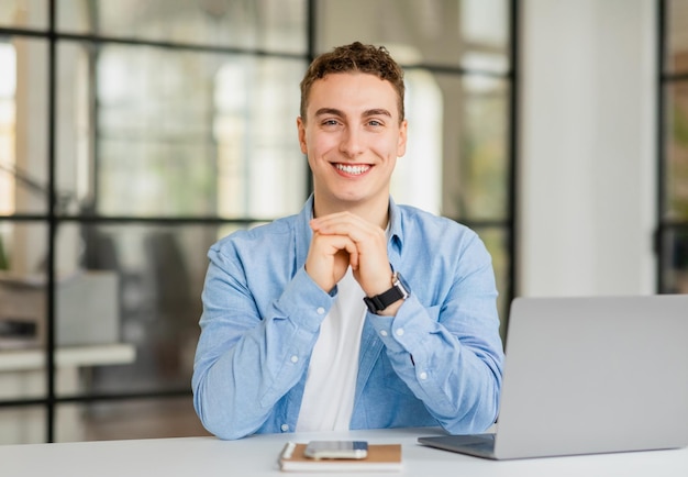 Positieve knappe jonge Europese man manager in casual met laptop aan tafel