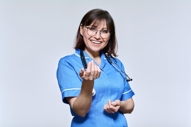 Positieve lachende verpleegster in blauw uniform kijkend naar camera op lichte studio achtergrond