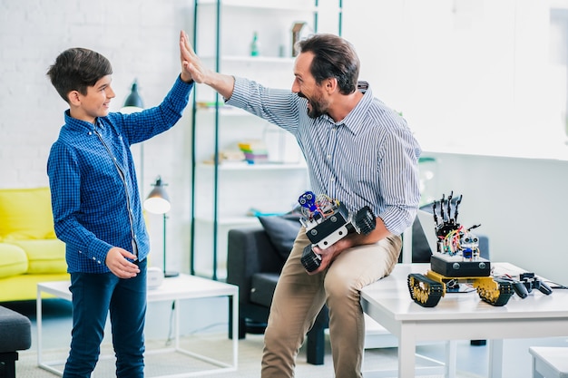 Positieve liefhebbende vader die zijn zoon high five geeft terwijl hij een robotapparaat vasthoudt