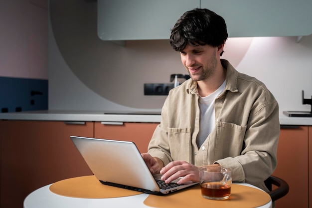 Positieve man die thuis online werkt op een laptop zit aan een tafel in de keuken en kijkt naar de dev