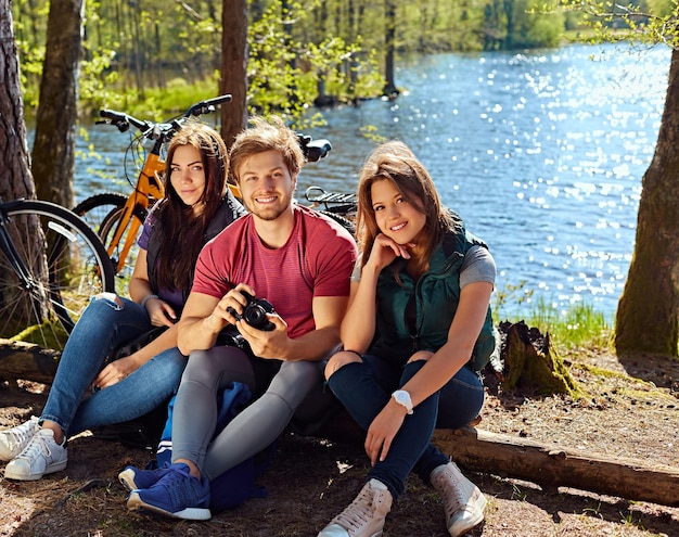 Positieve man en twee meisjes met behulp van een compacte digitale camera aan de kust van de wilde rivier na fietstocht.