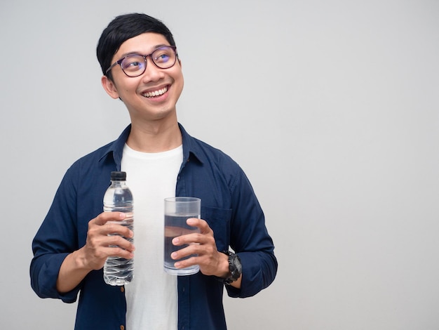 Positieve man houdt waterfles vast met glazen water, zachte glimlach die naar kopieerruimte kijkt