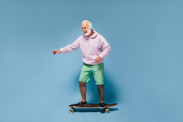 Positieve man in streetstyle-outfit die skateboard berijdt en naar muziek luistert