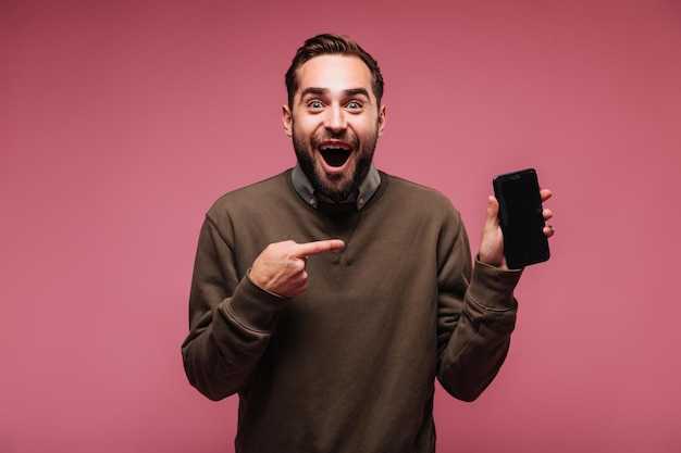 Positieve man in sweatshirt lacht en wijst met zijn vinger naar de telefoon