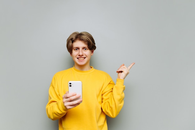 Positieve man met een smartphone in zijn handen staat op een achtergrond van een grijze muur