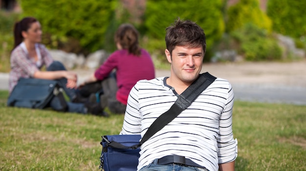 Positieve mannelijke student die op het gras met zijn schooltas ligt