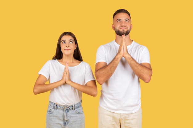 Positieve millennial Europese familie in witte T-shirts hopen of wensen en doen bidden gebaar kijken omhoog.