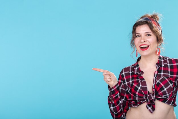 Positieve mooie jonge vrouw in een geruit vintage shirt kijken naar de camera en glimlachend poseren op een blauwe achtergrond. Advertentie ruimte