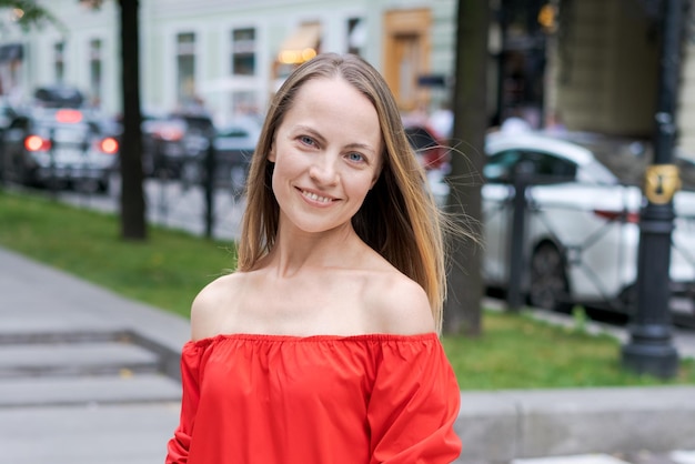 Positieve mooie vrouw in rode stands en glimlacht in de stad op straat