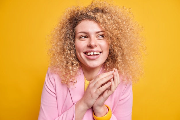 Positieve oprechte europese vrouw met krullend haar houdt handen bij elkaar heeft een gelukkige stemming happy