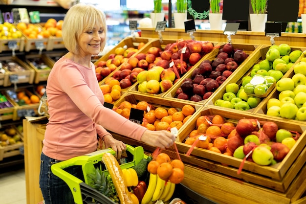 Positieve oudere dame die winkelt bij een enorme supermarkt die fruit koopt