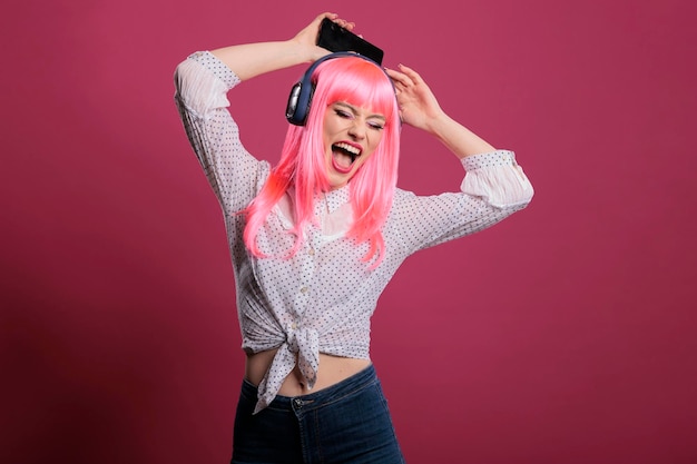 Positieve persoon met roze haar die plezier heeft met mp3-muziek, luisterend naar radioliedjes op een koptelefoon. Dansbewegingen doen en genieten van audiogeluid, ontspannen en gelukkig voelen. Coole stijl.