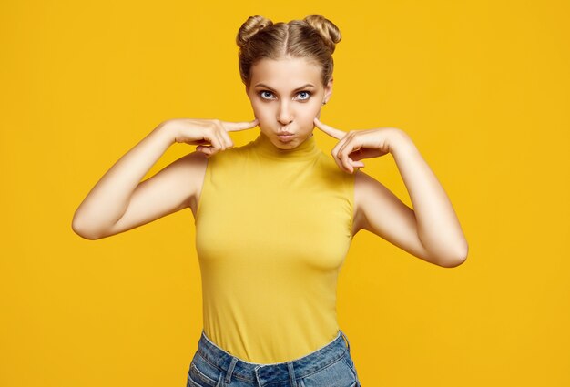 Positieve portret van prachtige blonde hipster vrouw model met krullend haar poseren op kleurrijke gele achtergrond in de studio