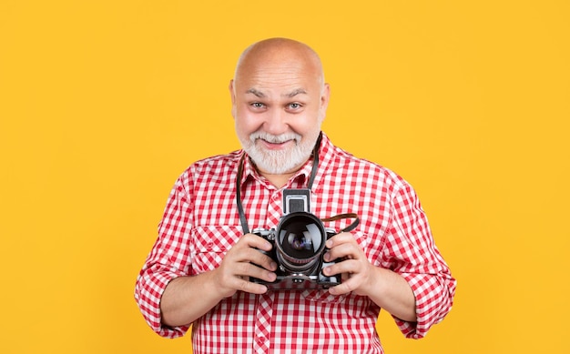 Positieve senior man met retro fotocamera op gele ondergrond