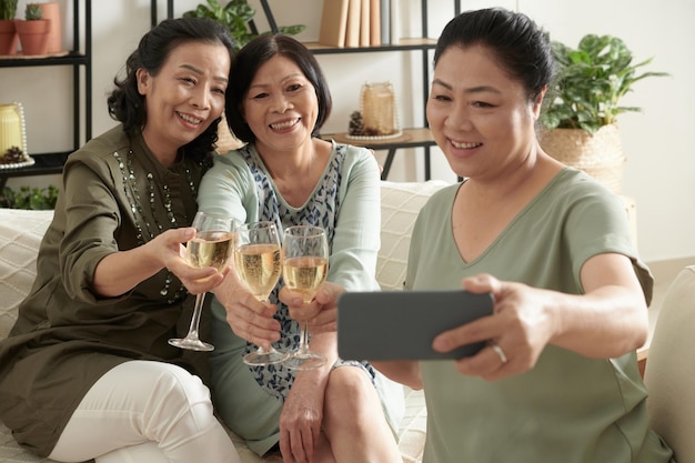 Positieve senior vrouw die selfie maakt met vrienden wanneer ze roosteren met wijnglazen