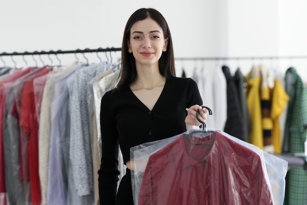 Positieve stomerij werknemer glimlacht met rode jas op hanger onder folie jonge brunette vrouw