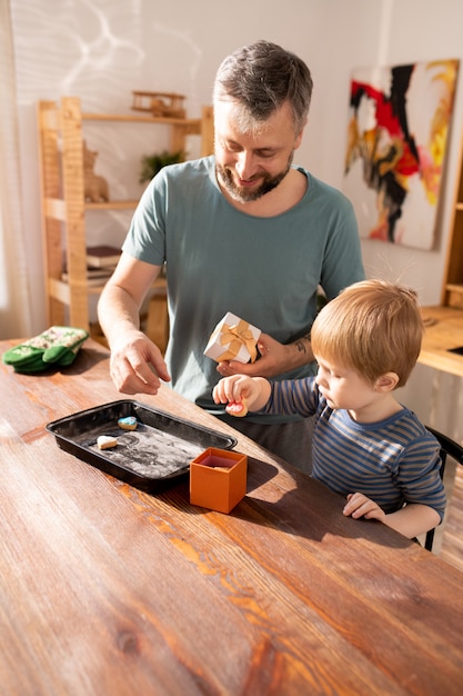 Positieve vader en zoon die koekjes zetten in giftdoos