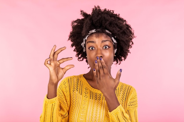 Positieve vrolijke donkere huid gekrulde vrouw vormt iets heel weinig met vingers toont kleine verminderde prijs of salaris gebaren niet groot object glimlacht toothily