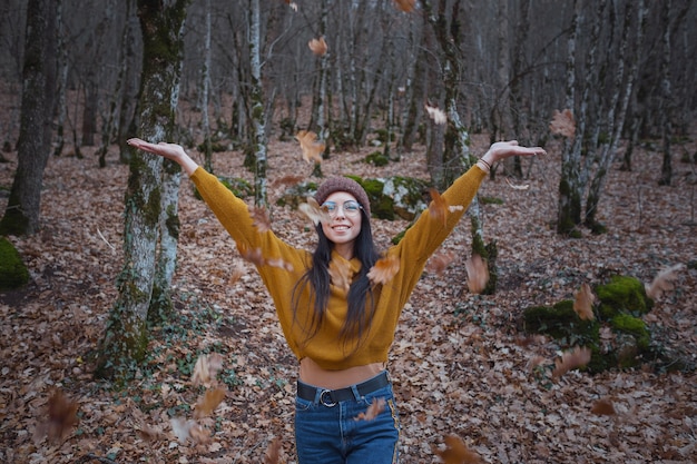 Positieve vrolijke vrouw geniet van de herfst in park of bos, draag gele trui en hoed, bril. Stemming gelukkig hipster meisje in de late herfst bos road trip