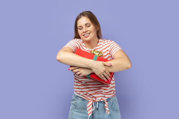 Positieve vrouw die een rode huidige doos omhelst die erg blij is met haar cadeau