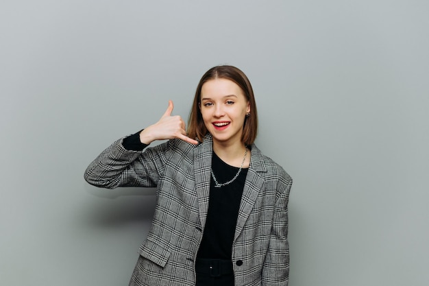 Positieve vrouw in een jas staat op een grijze achtergrond kijkt naar de camera met een glimlach op zijn gezicht