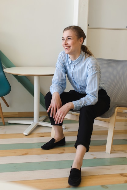 Positieve vrouw in formele kleding zittend op een stoel in kantoor