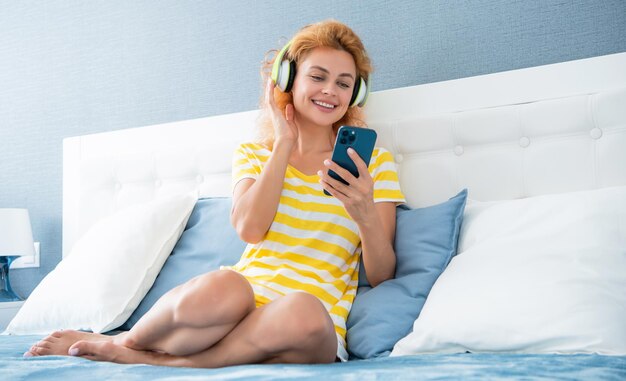 Positieve vrouw in koptelefoon chatten op telefoon Vrouw thuis chatten in koptelefoon