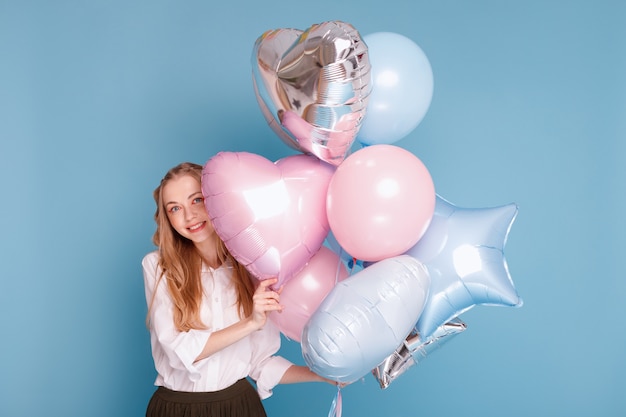 Positieve vrouw met ballonnen lachend op een blauwe ondergrond