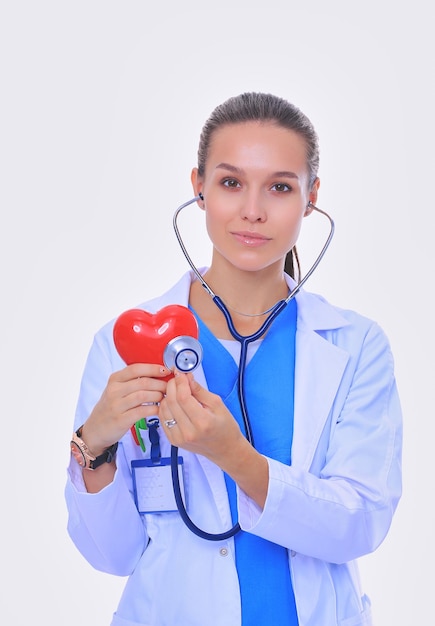 Positieve vrouwelijke arts die zich met stethoscoop en rood hartsymbool geïsoleerd bevindt Vrouw arts