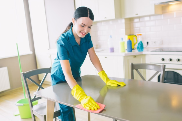 Positieve vrouwelijke reiniger kijkt naar beneden en maakt schoon aan tafel