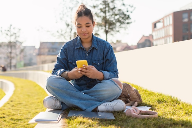 Positieve zwarte tienerdame die smartphone gebruikt en sms't op sociale media die pauze neemt van haar studie