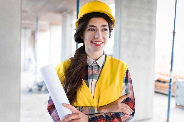 Photo positiv girl engineer at construction site with drawings in hand ive smile woman engineer builder stands at a construction site holding paper with drawings