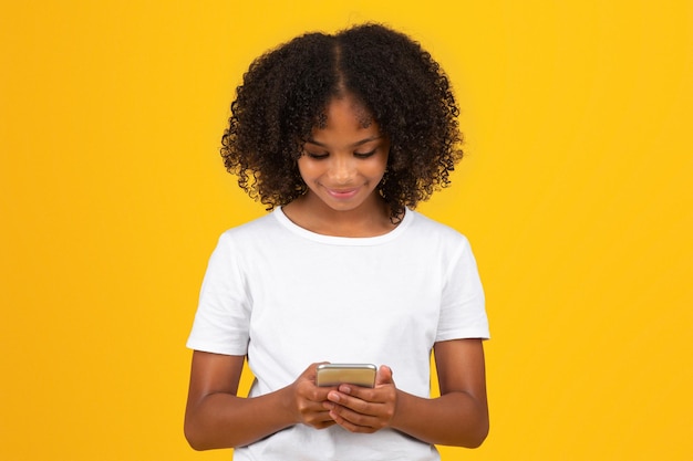 Positive adolescent black girl in white tshirt uses phone to chat in social networks