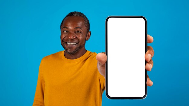 Positive adult african american man showing cell phone on blue