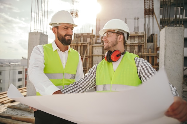 Positive adult men reading blueprint during work on construction